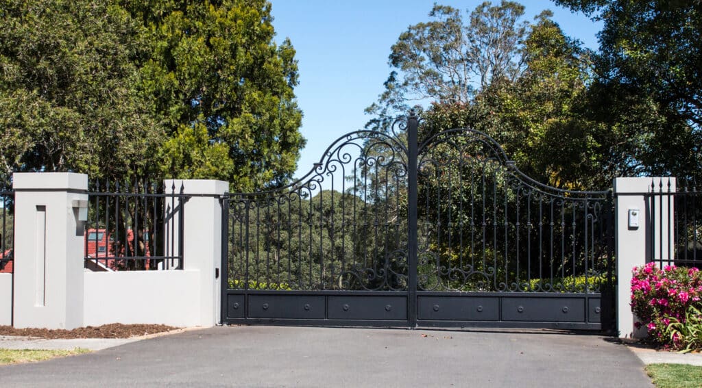 Ornamental wrought iron driveway gate with arched scrollwork between white pillars at a Southern California home